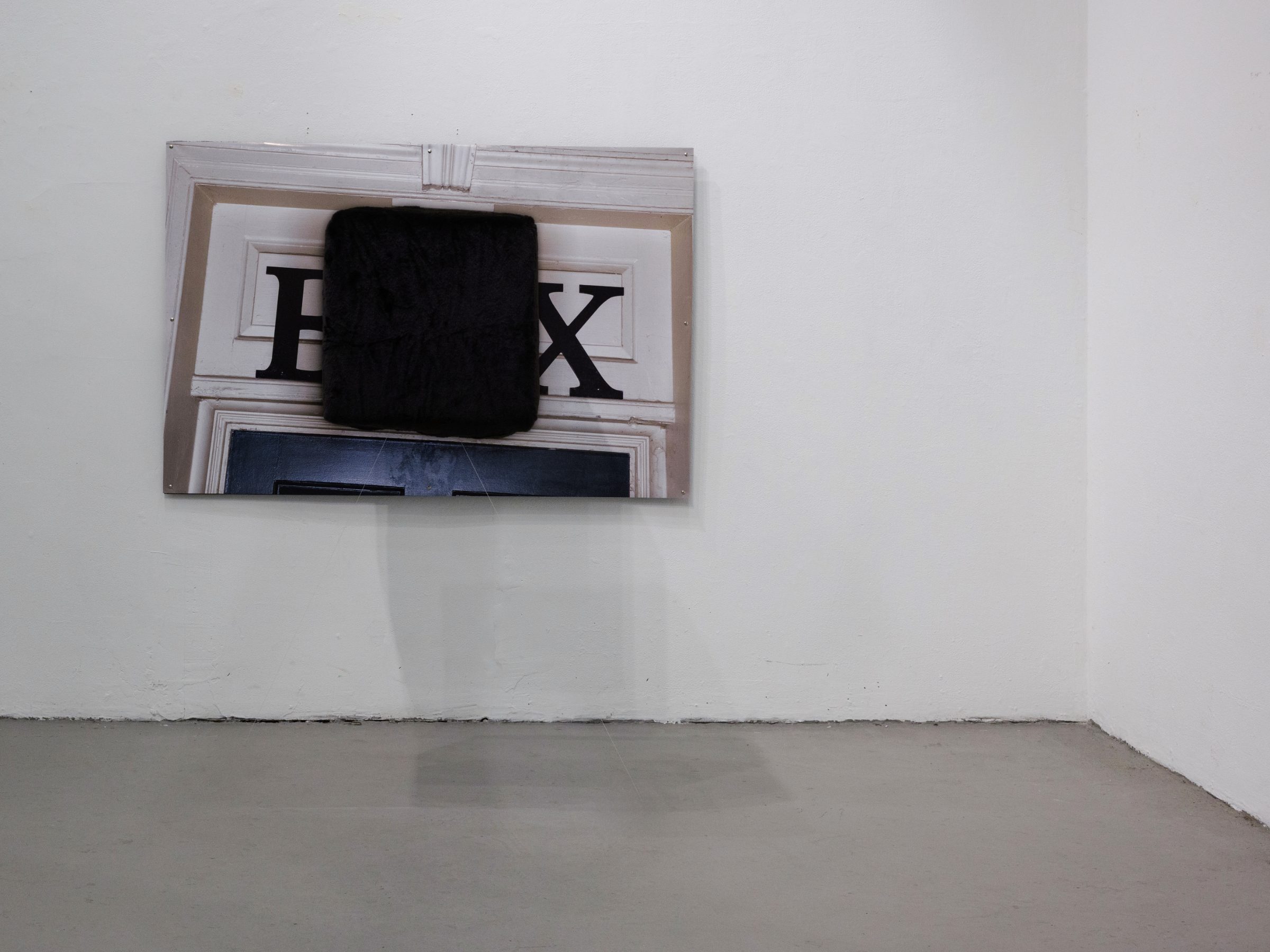 Installation view of 2nd hand art: the BOX/BOX/BOX print with a protruding black fur cube on a corner wall above a polished concrete floor.