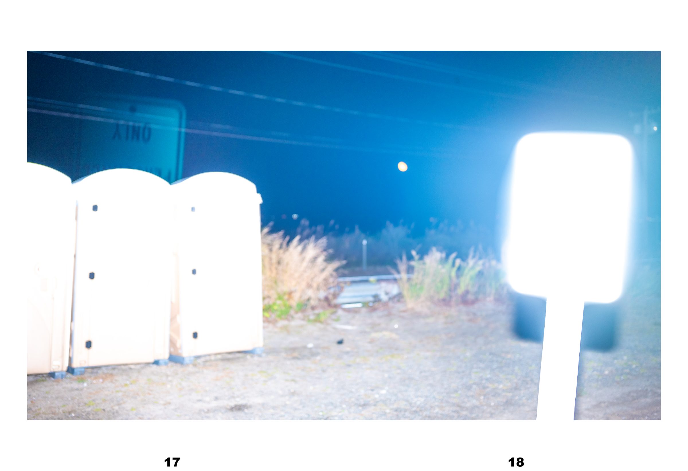 Spread: portable toilets beside a highway sign at night, lit blue, with a blown-out white light at right.