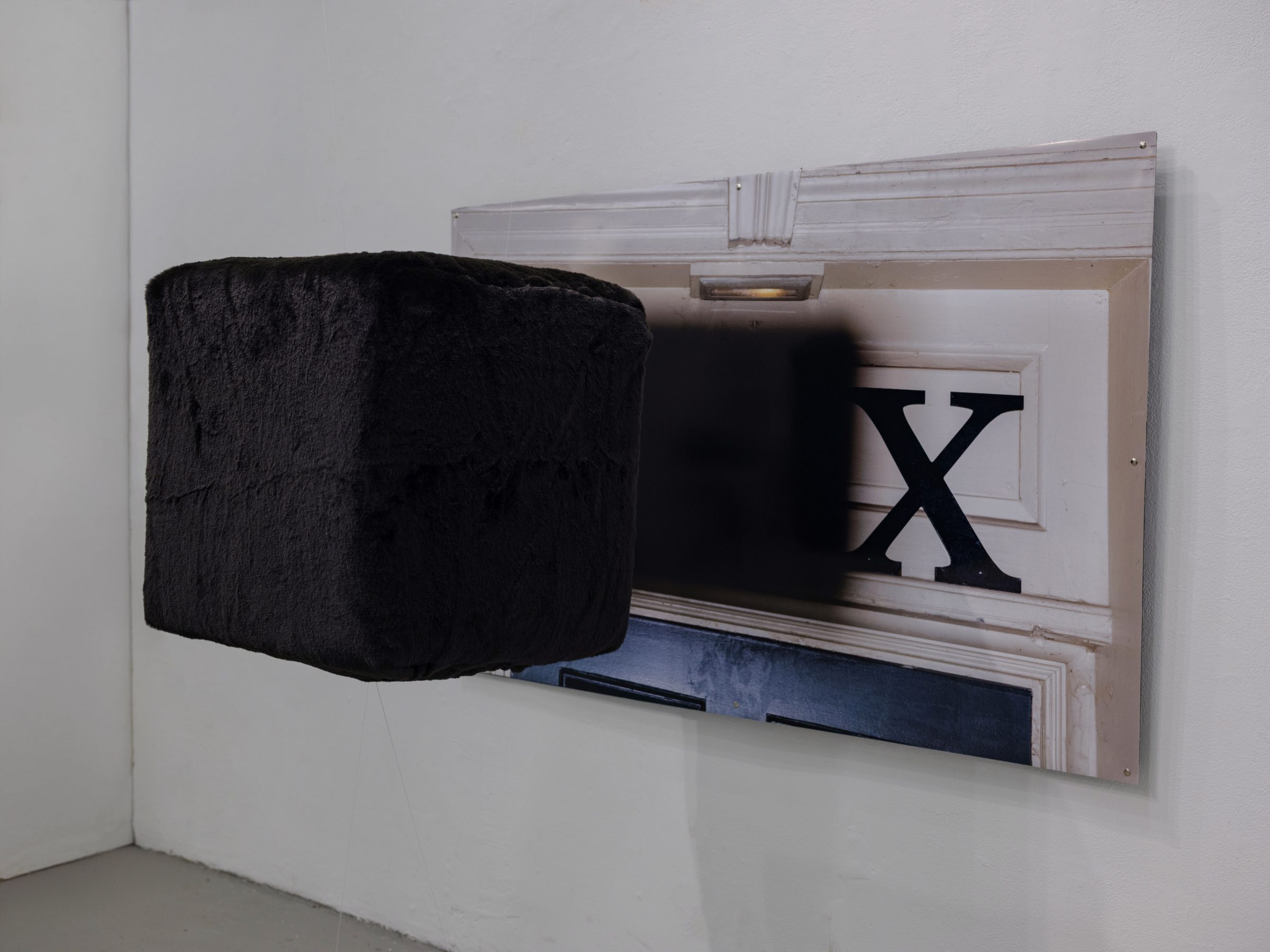 The BOX/BOX/BOX work seen from the side, the black fur cube projecting out from the printed door image on the corner wall.