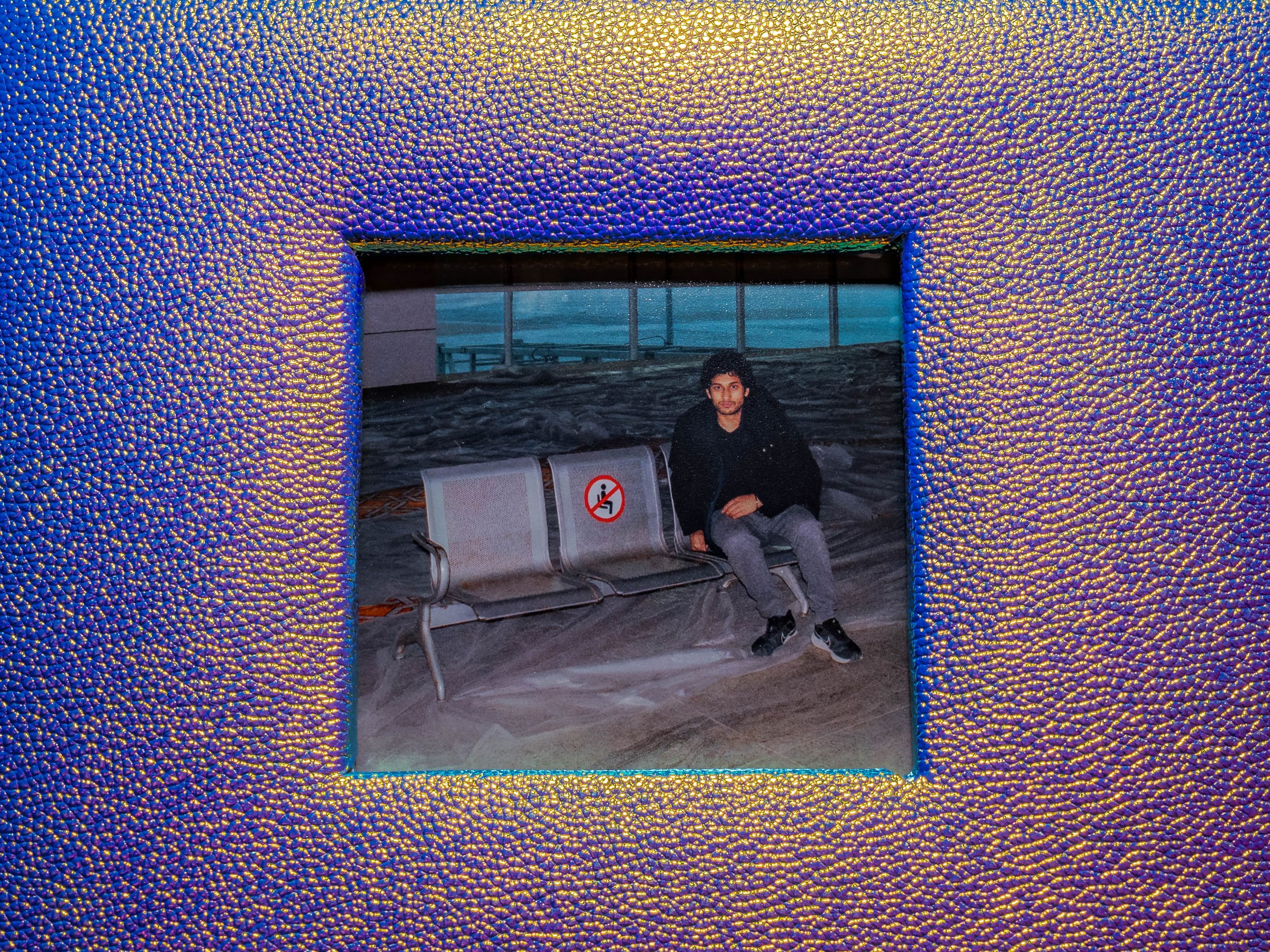 Detail: the small airport snapshot at the centre of the iridescent blue album cover, seen straight on.