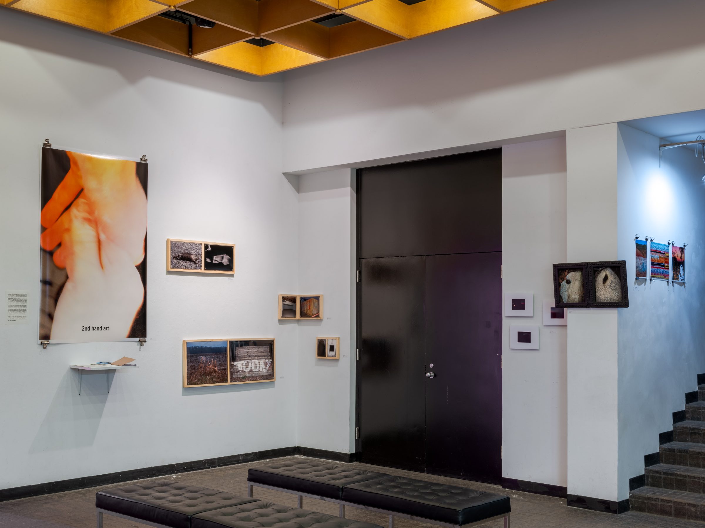 Installation view: the large orange hand poster titled 2nd hand art beside a dark doorway, with diptych boxes and tire-framed works around it.